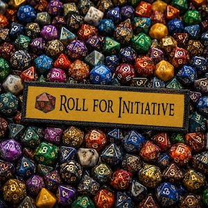 May include: A rectangular patch with a tan background and black border featuring the text "ROLL FOR INITIATIVE" and a small 20-sided die icon, resting atop a dense collection of multi-colored, glittery, and translucent polyhedral dice.