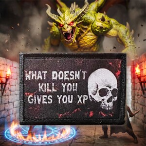 Könnte beinhalten: Ein rechteckiger schwarzer Stoffaufnäher mit einer weißen Totenkopf-Grafik auf der rechten Seite und dem weißen Text "WHAT DOESN'T KILL YOU GIVES YOU XP" auf der linken Seite, umrandet von einer genähten Kante entlang des gesamten Rechtecks.