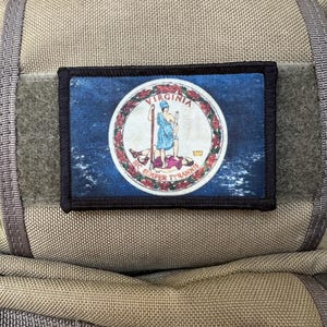 Könnte beinhalten: Ein schwarzer Patch mit blauem Hintergrund und einem weißen Kreis in der Mitte. Der Kreis enthält ein rotes und weißes Bild einer Frau, die einen Speer und eine Krone hält. Der Text "VIRGINIA" und "SIC SEMPER TYRANNIS" ist um den Kreis herum geschrieben.