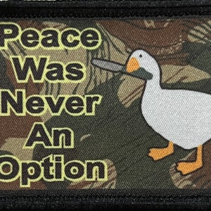 Könnte beinhalten: Eine weiße Gans mit orangefarbenem Schnabel und Füßen hält ein Messer. Die Gans befindet sich auf einem Tarnmusterhintergrund mit dem Text "Peace Was Never An Option" in gelben Buchstaben.