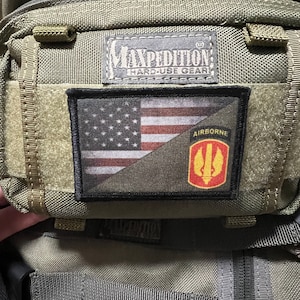 Op de afbeelding: Een groene Maxpedition Hard-Use Gear tas met een zwart-witte Amerikaanse vlag patch en een gele Airborne patch met een rood symbool.