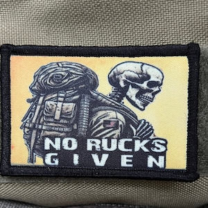Pode incluir: Um remendo preto e branco com um esqueleto carregando uma mochila. O texto "NO RUCKS GIVEN" está impresso no remendo.