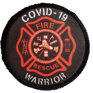 Op de afbeelding: Een ronde zwarte en rode patch met een brandweerembleem. Het embleem is een rood kruis met de woorden "FIRE" en "RESCUE" erin. De woorden "COVID-19" en "WARRIOR" staan rond het embleem.