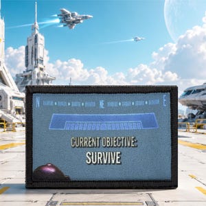 Könnte beinhalten: Ein rechteckiger Aufnäher mit schwarzem Rand und blauem, strukturiertem Hintergrund. Der Aufnäher zeigt oben eine digitale Kompassgrafik und mittig den weißen Text "CURRENT OBJECTIVE: SURVIVE" sowie ein kleines violettes Kugel-Symbol.
