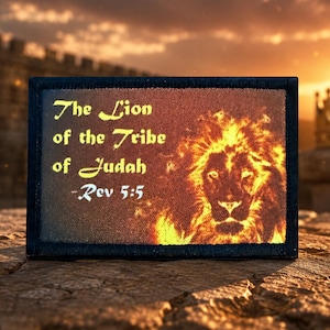 May include: A rectangular patch with a black border featuring a graphic of a lion's face surrounded by orange and yellow flames. The text reads: The Lion of the Tribe of Judah -Rev 5:5. The design is printed on a textured fabric surface.