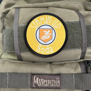 Peut inclure: Un sac à dos vert Maxpedition Hard-Use Gear avec un patch Stamin-Up Soda jaune et noir.