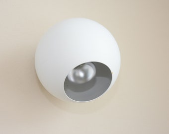 May include: A white spherical wall light fixture with a round opening revealing a light bulb.