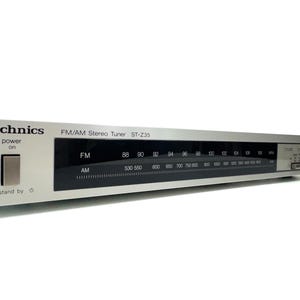 Puede incluir: Sintonizador estéreo FM/AM Technics ST-235 plateado. Cuenta con una pantalla negra con indicadores de frecuencia FM y AM. Incluye un botón de encendido y un mando de sintonización. El texto "Technics" es visible.