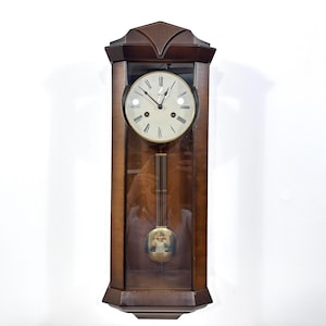 May include: A vintage wooden wall clock with a pendulum. The clock has a rectangular frame with a glass front, a round clock face with black numerals, and a decorative pendulum. The clock is made of dark brown wood.