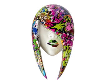 May include: A white ceramic sculpture of a woman's face with a colorful, abstract design on the hair. The design features bright pink, green, and blue colors.