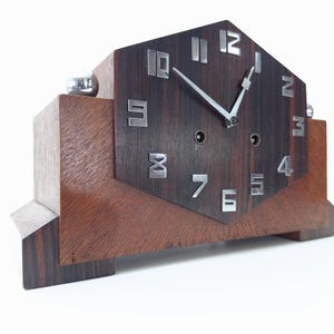 May include: A dark wood clock with a hexagonal face and silver hands. The clock has Roman numeral markings and is sitting on a wooden base.