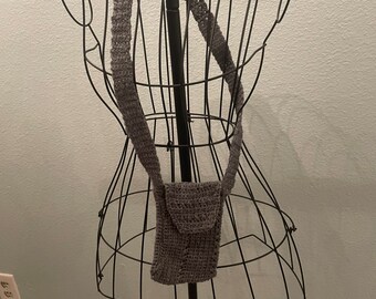 May include: A grey crocheted crossbody bag with a long strap hanging on a black metal mannequin.