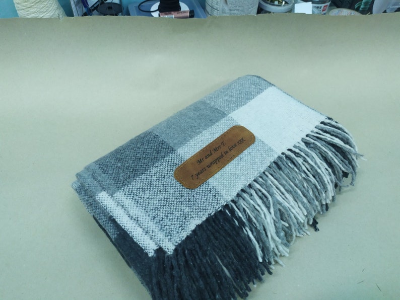 May include: A gray and white plaid throw blanket with a brown leather tag that says "Mr and Mrs T 7 years wrapped in love xxx".