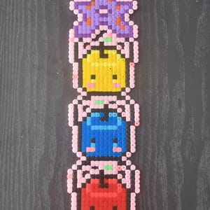 May include: A vertical stack of four colorful pixel art figures. The top figure is purple with green accents, followed by yellow, blue, and red figures. Each figure has a pink outline and a small green accent.