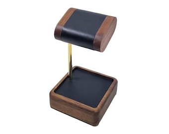 May include: A wooden watch stand with a black leather top and a gold metal rod. The stand has a square base and a rectangular top.