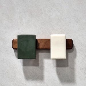 Pode incluir: Um saboneteira de madeira com duas barras de sabão, uma verde e uma branca.