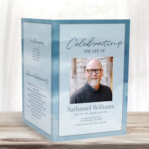 May include: A blue and white watercolor funeral program with a photo of a man wearing glasses. The program includes the text "Celebrating the Life of Nathaniel Williams" and the dates "May 15, 1971 - January 22, 20XX".