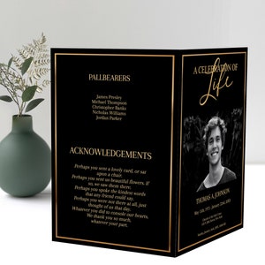 Front and back of a funeral program standing up. A large photo is on the front of the program with gold text, gold text is also on the back of the pamphlet. Black background, with gold border.