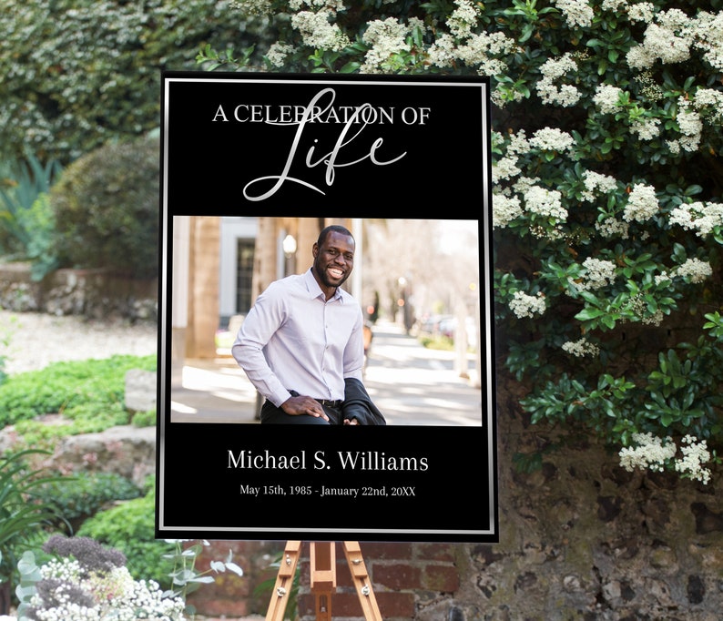Op de afbeelding: Een zwart en zilveren ingelijst bord met de tekst "A Celebration of Life" in zilveren schrift. Het bord bevat ook een foto van een lachende man, de tekst "Michael S. Williams" en de data "May 15th, 1985 - January 22nd, 20XX".