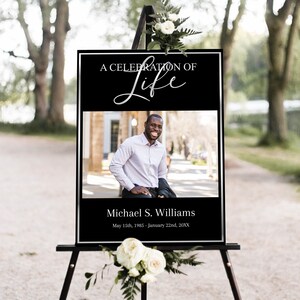 Op de afbeelding: Een zwart-wit bord met een zilveren inscriptie die "A Celebration of Life" luidt, met een foto van een man en de tekst "Michael S. Williams, May 15th, 1985 - January 22nd, 20XX".