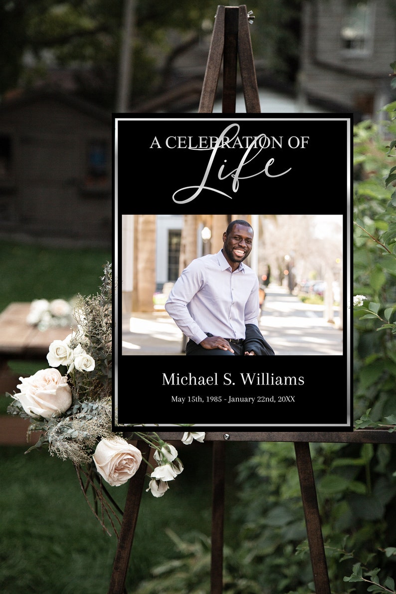 Op de afbeelding: Een zwart-wit gedenkteken met een zilveren rand. Het bord heeft de tekst "A Celebration of Life" in een zilveren handschrift. Een foto van een man is in het midden van het bord. De tekst onder de foto luidt "Michael S. Williams" en "May 15th, 1985 - January 22nd, 20XX".