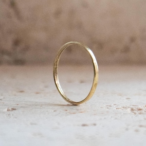 Könnte beinhalten: Ein zarter, dünner Goldring steht vor einem neutralen Hintergrund. Das schlichte Design und die polierte Oberfläche des Rings reflektieren das Licht und betonen seine kreisförmige Form. Ein minimalistisches Schmuckstück.