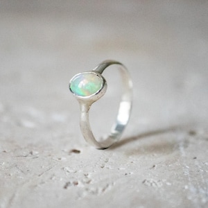 Puede incluir: Un delicado anillo de plata con una pequeña piedra de ópalo redonda y blanca.