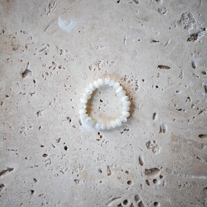 May include: A white beaded bracelet made of small, round, iridescent beads.