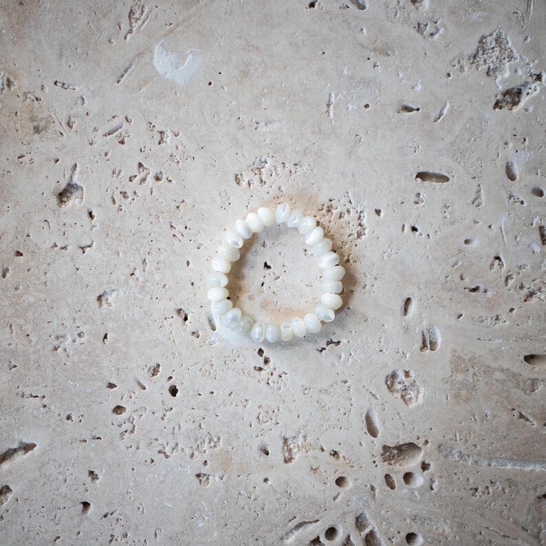 May include: A white beaded bracelet made of small, round, iridescent beads.