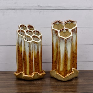 May include: Two ceramic vases with a honeycomb design. The vases are brown with white and yellow glaze, and have a wavy base. The vases are approximately 8 inches tall.