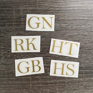 May include: Five white squares with gold lettering spelling out the words "GN", "RK", "HT", "GB", and "HS".