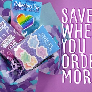 May include: A selection of stickers, a collector's pin, and a mystery sticker pack are presented in a decorative box. The pin is heart-shaped with a rainbow design. The text "SAVE WHEN YOU ORDER MORE" is visible.