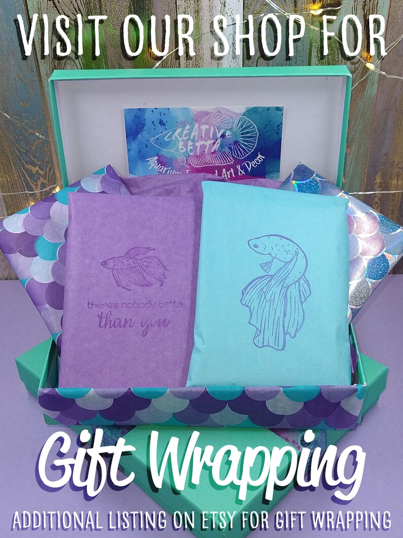 May include: A teal gift box with purple and teal tissue paper. Two wrapped packages, one purple and one teal, are inside, each with a fish illustration. The text "Gift Wrapping" is displayed in white, with the words "Visit Our Shop For" above.