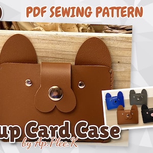 Peut inclure: Un porte-cartes en similicuir marron en forme de chiot avec deux oreilles, une fermeture à pression centrale et deux petits clous métalliques pour les yeux. Le texte "PDF SEWING PATTERN" et "Pup Card Case by Ap.Plee.K" est visible.