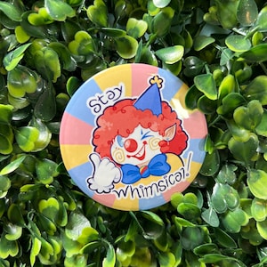 Könnte beinhalten: Ein runder Knopf mit einem Comic-Clown mit roten Haaren, einem blauen Hut und einer blauen Schleife. Der Clown zeigt den Daumen nach oben und der Knopf sagt "Stay Whimsical!" in gelben Buchstaben auf einem rosa und blauen Hintergrund.