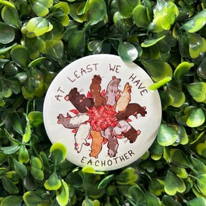Könnte beinhalten: Ein weißer Knopf mit einem Kreis aus Comic-Ratten, die ein rot-weiß gestreiftes Band umgeben. Der Text "At least we have each other" ist um den Kreis der Ratten geschrieben.