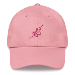 Peut inclure: Casquette de baseball rose avec un motif brodé rose en forme de cœur avec une flèche pointant vers le haut.