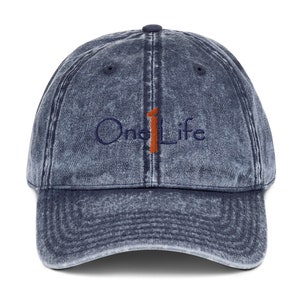 May include: A blue denim baseball cap with a distressed look. The cap has an embroidered logo that says "One Life" with a large orange number "1" in the middle.