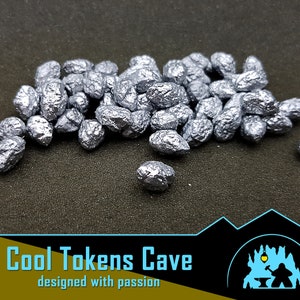 Könnte beinhalten: Ein Haufen silberner Metallnuggets, die an Steine oder Edelsteine erinnern, auf einem dunkelgrauen Hintergrund. Cool Tokens Cave, entworfen mit Leidenschaft.