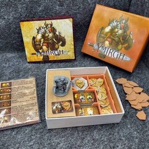 Puede incluir: Una caja blanca con una figura en miniatura gris en su interior. La caja tiene un inserto marrón con compartimentos para las piezas del juego. La caja está etiquetada como "Ymirgh" y tiene una imagen de un guerrero en la tapa. También hay fichas de cartón marrón y un conjunto de instrucciones.