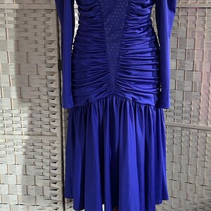 May include: A royal blue long-sleeved dress featuring a sweetheart neckline, gathered shoulder detailing, and a central panel with a subtle dot pattern. The bodice is heavily ruched, transitioning into a pleated, knee-length skirt silhouette.