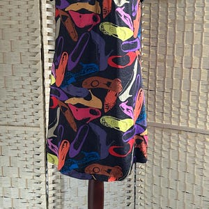 May include: A black dress with a scoop neckline and short sleeves, adorned with a colorful shoe print. The shoes are in various colors, including orange, purple, pink, and yellow. The dress is displayed on a mannequin.