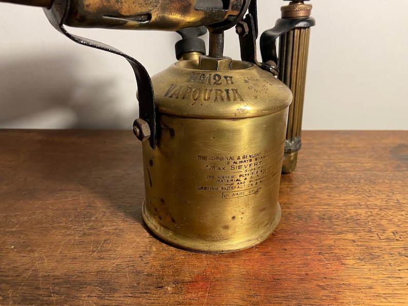 Pode incluir: Um ma&ccedil;arico vintage de lat&atilde;o com uma pega preta e um r&oacute;tulo que diz "12H JAPOURIA THE ORIGINAL & BENLINE IS ALWAYS STANDARD MAX SIEVERT"