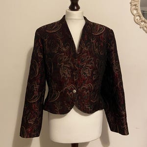 May include: A cropped, black and burgundy blazer with a paisley pattern. The blazer has a single button closure and long sleeves.