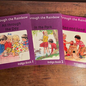 May include: Three vintage children's books titled "Through the Rainbow" with purple covers. The books are "All through the Day", "In the Park", and "Sea and Sand". Each book features colorful illustrations of children and scenes.
