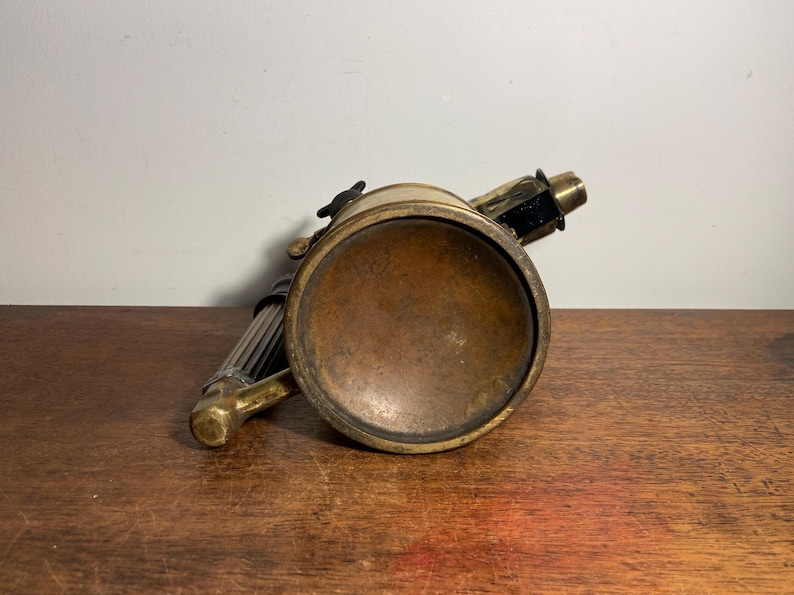 Pode incluir: Um ma&ccedil;arico vintage de lat&atilde;o e preto com um corpo redondo de lat&atilde;o e uma al&ccedil;a longa e fina. O ma&ccedil;arico est&aacute; sobre uma superf&iacute;cie de madeira.