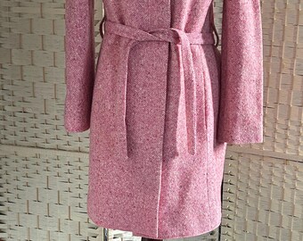 Puede incluir: Un abrigo de tweed rosa con cinturón a juego, exhibido en un maniquí de madera. El abrigo tiene un diseño clásico con cuello con solapas y mangas largas. El abrigo mide aproximadamente 102 cm de largo.