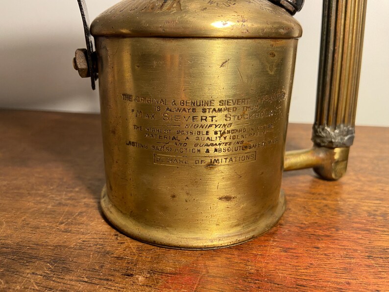 Pode incluir: Um ma&ccedil;arico de solda Sievert vintage de lat&atilde;o com uma pega longa e canelada. O ma&ccedil;arico tem um r&oacute;tulo que diz "The Original & Genuine Sievert" e "Beware of Imitations".