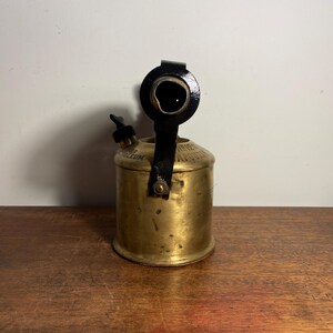 Pode incluir: Um ma&ccedil;arico de lat&atilde;o vintage com uma al&ccedil;a de metal preto e um bico. O ma&ccedil;arico tem um r&oacute;tulo que diz "Superior Petroleum".