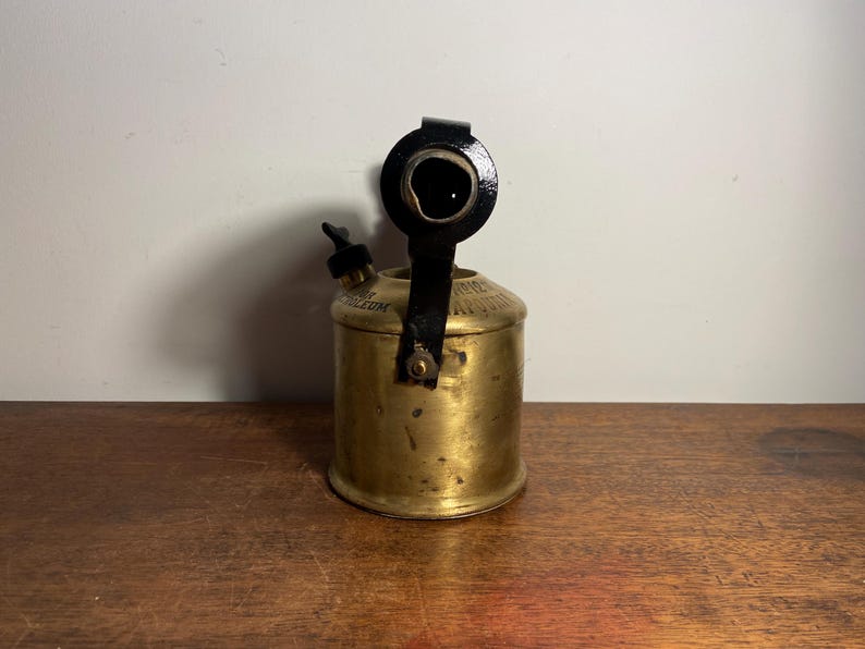 Pode incluir: Um ma&ccedil;arico de lat&atilde;o vintage com uma al&ccedil;a de metal preto e um bico. O ma&ccedil;arico tem um r&oacute;tulo que diz "Superior Petroleum".